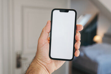 Tourist in hotel bedroom holding smartphone with blank mockup screen for booking and reservation app