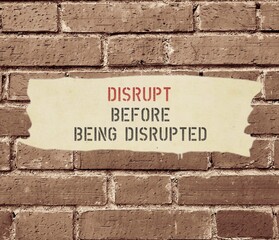 Old time brick wall background with text inscription DISRUPT BEFORE BEING DISRUPTED, means business must start to transform strategically to advance technology and digital capability to deal with it