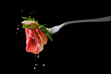 Sprinkling piece of beef carpaccio on fork with lemon juice over black background