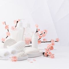 Cosmetic products for body care, cleansing skin in white bottles, branch of spring pink sakura flowers, toiletry in elegant light bathroom interior in geometric futuristic asian style, square.