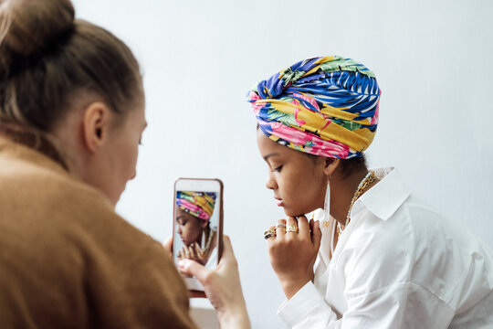 Fashion designer taking photo of young African woman model with colorful shawl on her head and ethnic jewelry. Fashion clothes studio, local brand, small business