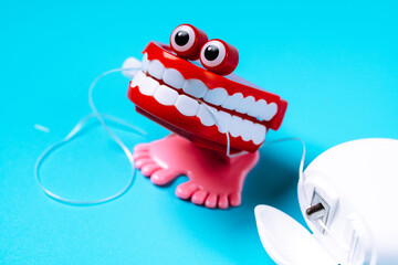 Funny toothed toy holding dental floss lying on a blue background. Dental care concept. - obrazy, fototapety, plakaty