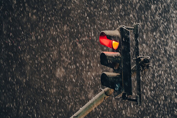Red traffic light on a pole during a winter night with massive snowfall. Transportation...