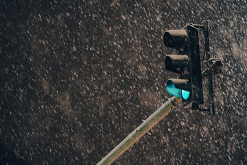 Green traffic light on a pole during a winter night with massive snowfall. Transportation...
