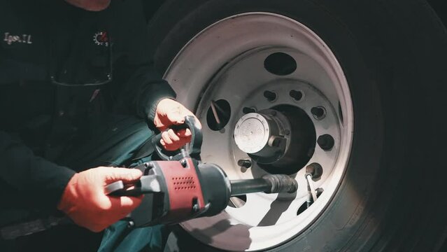 mechanic using impact wrench to tight down lug nuts of a big tire from a trailer