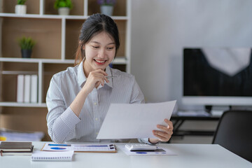 Young black-haired asian female worker working in office with financial documents and laptop calculating company annual budget accounting.