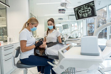 dentist with help of an assistant conducts a professional examination of patient's oral cavity.