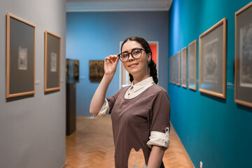 Arts exhibition. Portrait of young Caucasian pretty woman wearing glasses smiling. Student visiting...