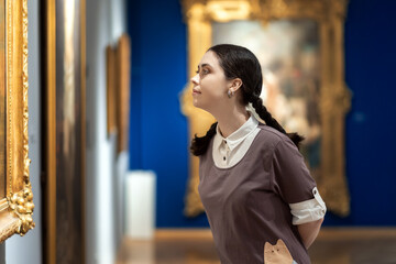 Side view of young Caucasian pretty woman contemplates ancient artefacts. Student visiting arts...