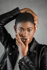Portrait of Black woman with hands touching head and face against gray wall