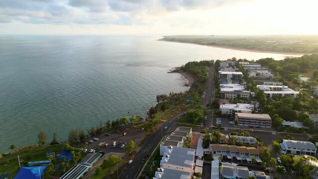 Aerial Drone Luxurious Property in residential neighbourhood suburb. Birds eye view of house roofs Tropical greenery palm trees outdoor public pool. Skyline of ocean and beach dusk Nightcliff