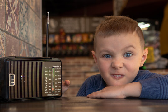 Charming grimacing boy at a table in a cafe with an old vintage radio
