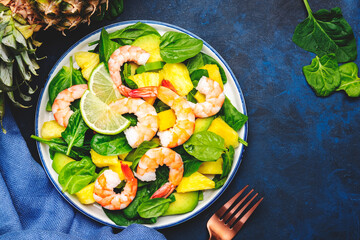 Shrimp pineapple salad with spinach, avocado and lime on blue kitchen table background, top view. Healthy vegetarian eating, balanced, clean diet food, weight loss dish