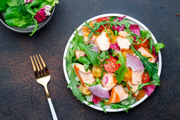 Grilled salmon fish salad with tomato, cucumber, arugula, radicchio, red onion and lettuce with lemon and sesame seeds. Brown table background, top view