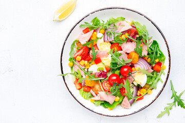 Fish tuna and fresh vegetables salad with cherry tomatoes, red onion, eggs, corn, paprika, lettuce, radicchio and arugula. White table background, top view