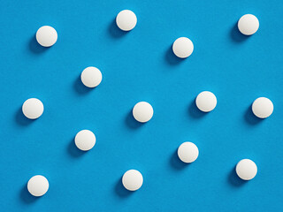 White round medical pills on blue background. Medical and pharmaceutical treatment concept.