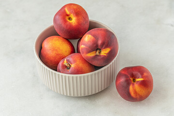 ripe sweet nectarines in a ceramic bowl on a white marble surface