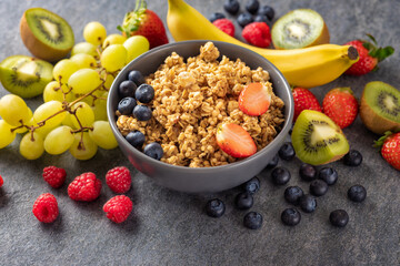 Bowl with homemade granola and various fruits for cooking tasty and healthy breakfast on dark background