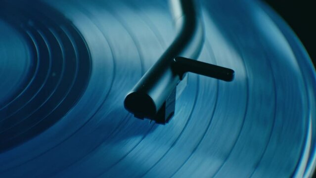 Super close up on turntable stylus touching vintage blue vinyl. Tone arm with needle, cartridge and stylus play music. 
