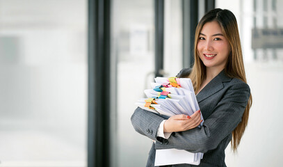 Beautiful businesswoman carrying a pile of documents standing at office, smiling to camera.