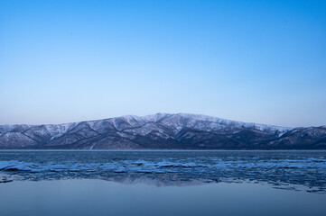 雲の無い青空の下、凍った湖の向こうに見る雪山。