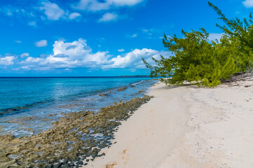 A view along a sandy the beach with rocky shore on the island of Eleuthera, Bahamas on a bright sunny day