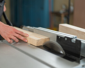 Close-up of a man cutting a wooden board on a circular machine.