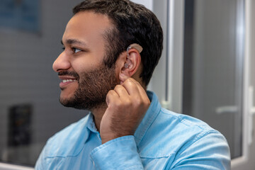 Smiling young man holding a hearing aid