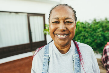 Happy african senior woman smiling on camera with house background - Main focus on nose