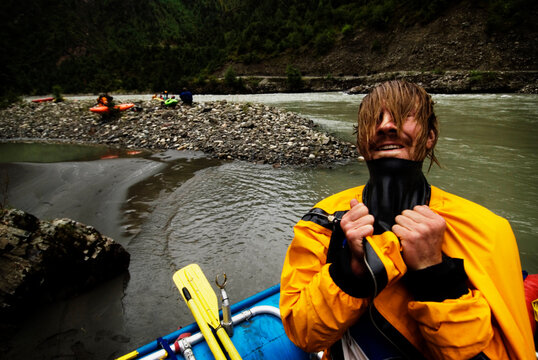 A young male rafter pulls his head through the gasket on his drysuit during a whitewater rafting trip in Western China.