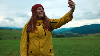 Video call. Happy traveler hiker girl in bright sportswear takes a selfie photo on a smartphone on top of a mountain on a summer day