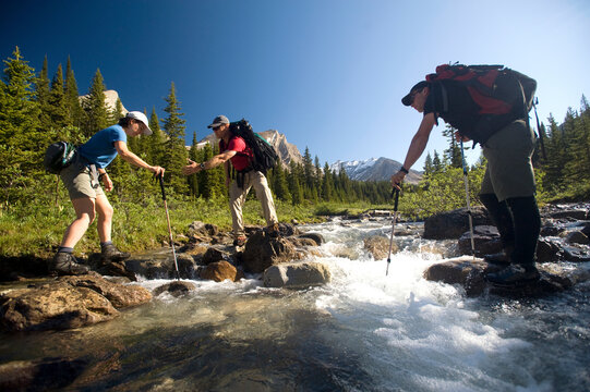 Two backpacking guides help a woman client across a creek in Banff NP Alberta Canada