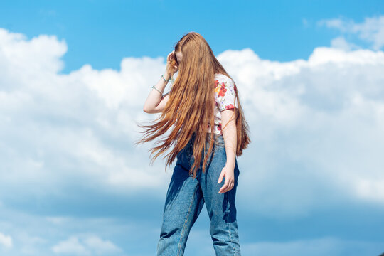 Teen ginger girl with long hair standing on the blue cloudy sky