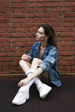 Girl in jeanscoat, bodysuit sneakers sits on a baseball court