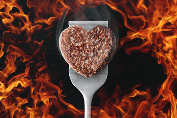 heart shaped beef burger patty on a grilled spatula. dark background place for text. valentines day celebration concept - 566210147