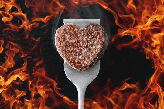heart shaped beef burger patty on a grilled spatula. dark background place for text. valentines day celebration concept