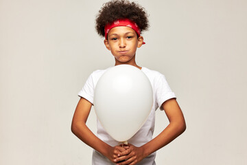 Teenage boy of african aethnicity blowing cheeks holding white mockup balloon with blank copy space...