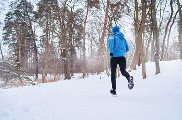 Healthy lifestyle. Jogging outdoors. Young strong man is running at snowy park.