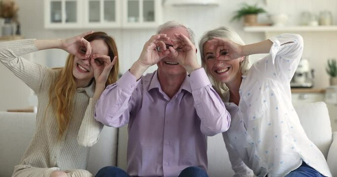 Multi generational family have fun, laughing, fooling staring at camera through joined fingers showing eyeglasses shape, advertise glasses or lenses store, vision check up professional clinic services
