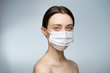 Portrait of a young beautiful woman in a medical mask on a white grey background.