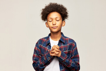 Studio image of cute african american teen boy kid praying for winning school competition or making...