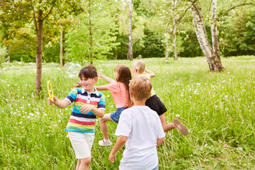 Obraz premium Multiracial children playing with soap bubbles in grass