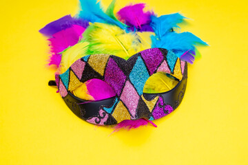 Venetian carnival mask in the style of Harlequin with multi-colored feathers on a yellow background.