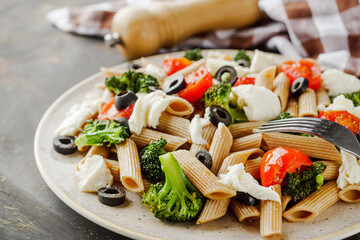 delicious penne wheat pasta with tomatoes, broccoli and mozzarella on a dark background