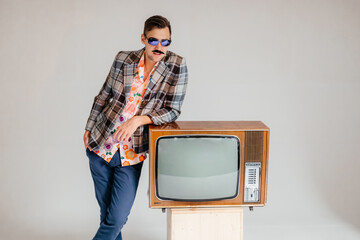Back in time 90s 80s lifestyle concept. Studio footage of stylish cheerful young man in vintage retro jacket with antique old tv, candy-colored fashions, creativity, emotions, facial expression