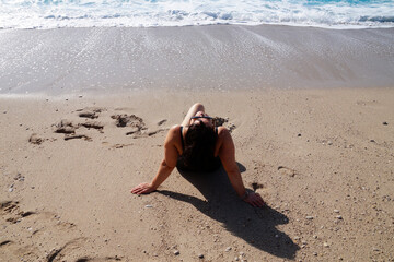 curvy woman sunbathing on the beach with her head thrown back to the sun