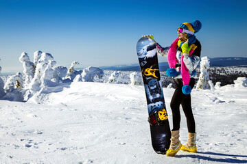 Girl snowboarder enjoys the ski resort. Beautiful woman in winter outfit is posing with snowboard...