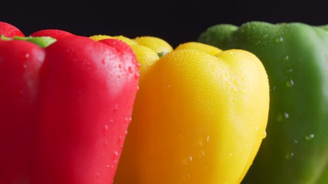 Green, red and yellow wet bell pepper rotated on black background. Mixed fresh colorful Bell Peppers wet, drip, water, dripping