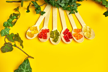 Flat lay composition with colored healthy vegan gummy bears  in eco wooden spoon with green leaves...