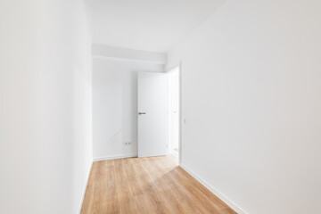 Empty narrow room with laminate flooring and newly painted white wall in refurbished apartment with corridor leading to other rooms. Repair and construction concept.